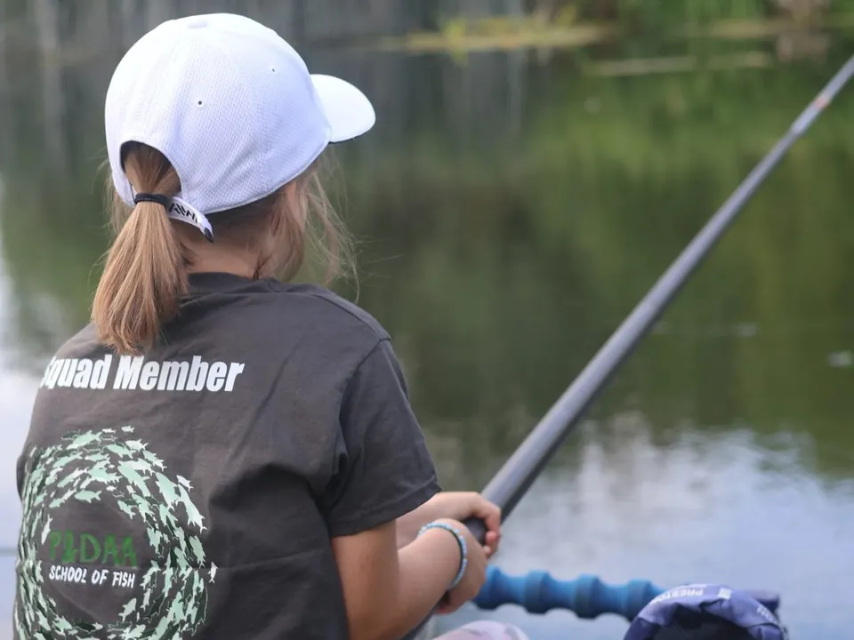 A junior in a Squad Member shirt fishing a pole