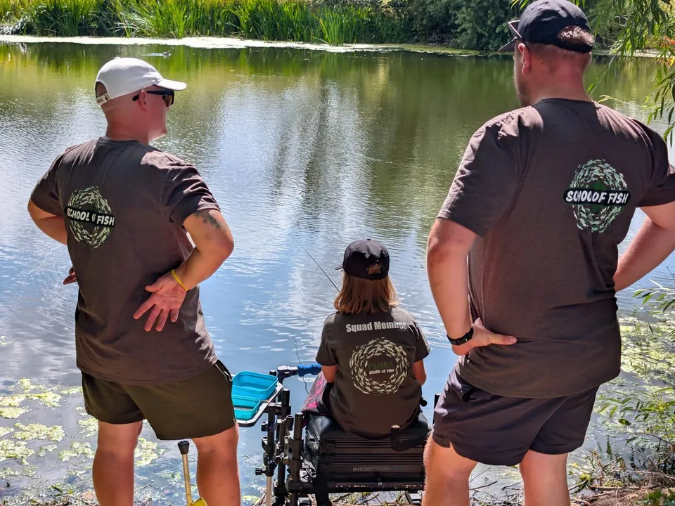Two coaches watching over a junior angler at a summer session