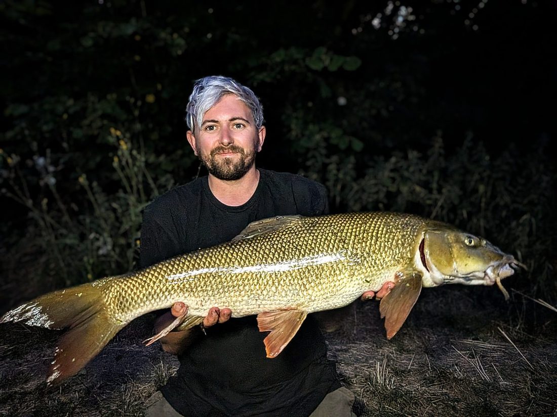 Jake Cunnington holding a 12lb barbel at Elton Fishery in the dark